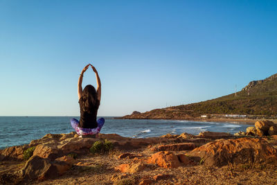 Woman standing on rock by sea against clear blue sky