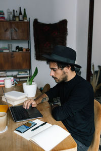 Side view freelancer sitting at table and typing on laptop while working on project in cozy home office