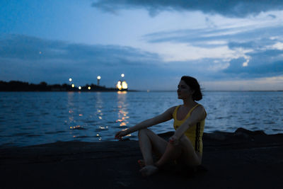 Woman sitting in sea against sky