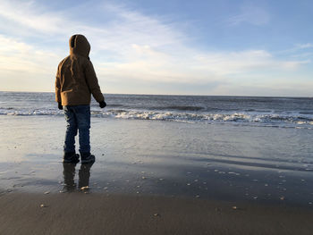 Rear view of child walking at beach against sky