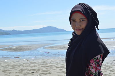 Portrait of woman standing at beach against sky