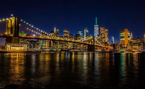 Illuminated bridge over river by buildings against sky at night