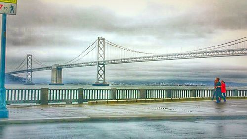 Rear view of suspension bridge against cloudy sky