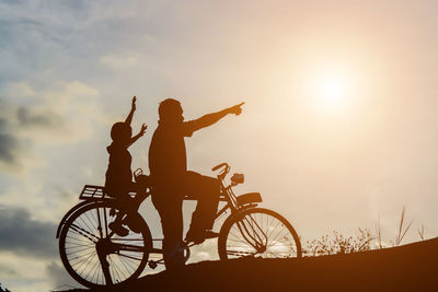 Silhouette people riding bicycle against sky during sunset