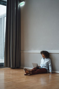 Thoughtful businesswoman with laptop sitting on floor in office