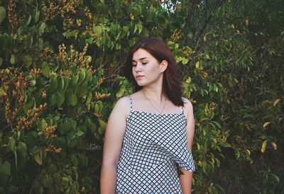 Thoughtful young woman standing against trees