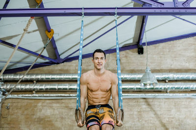 Smiling man in shorts exercising with gymnastic rings in health club