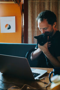 Man kissing cat while sitting on table