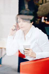 Woman talking over smart phone in cafe seen through window