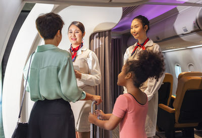 Two young asian female flight attendants in suit uniform stood at the plane's entry, l