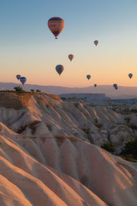 Hot air balloons flying over land against sky during sunset