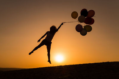 Silhouette woman with balloons flying against clear sky during sunset