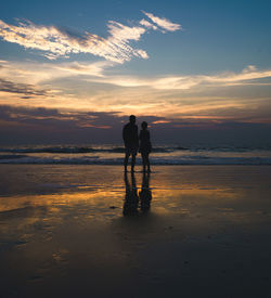 Silhouette couple standing on beach against sky during sunset