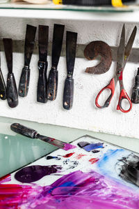 Various chisels and scissors arranged on wall near table with paints on workplace in engraving workshop