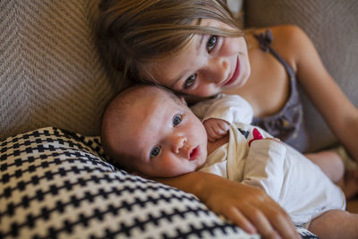 Portrait of girl with baby girl lying on sofa at home