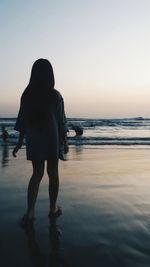 Rear view of woman standing on beach during sunset