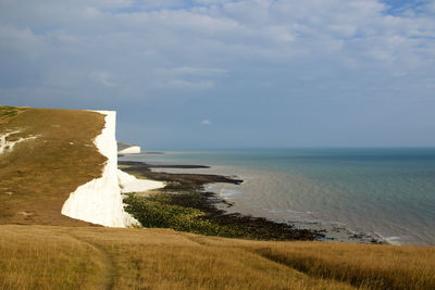 Scenic view of cliff by sea against cloudy sky