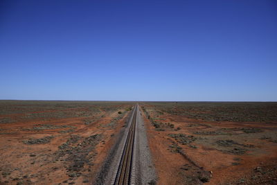 Scenic view of railroad tracks on field against clear blue sky