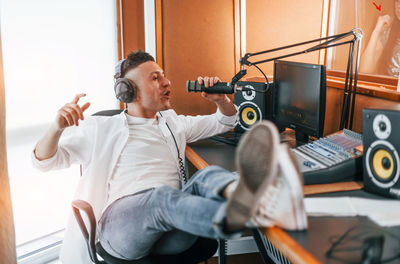 Talks and uses mic. young man is indoors in the radio studio is busy by broadcast.