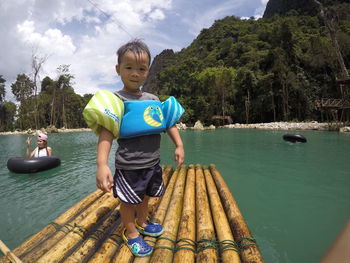 Portrait of boy standing wearing water wings while standing on pool raft against sky