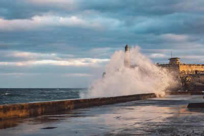 Sea waves splashing on shore against sky