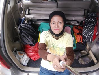 High angle portrait of young woman leaning on car trunk