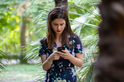 Young woman using mobile phone while standing on tree