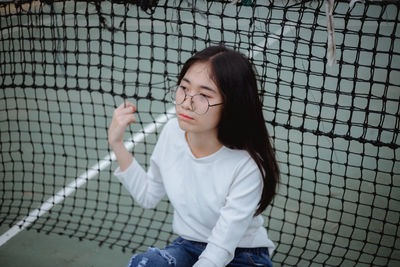 Young woman sitting against tennis net