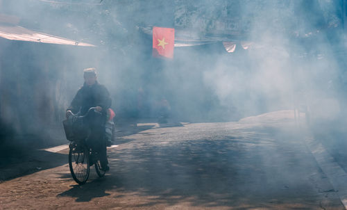 Mature man riding bicycle on road with smoke