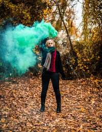 Young woman holding distress flare while standing in forest during autumn