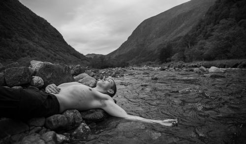 Man lying on rocks by mountains against sky