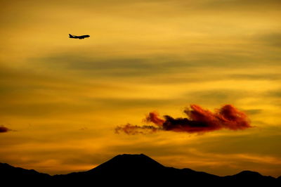 Silhouette airplane flying against orange sky