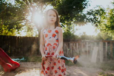Young girl looking away while playing in back yard with garden hose