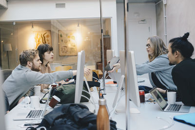 Female computer programmer showing digital tablet to colleagues at desk in office