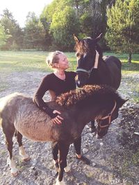 Smiling woman stroking horses while standing at ranch