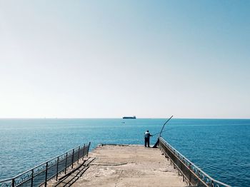 Rear view of man fishing on pier against sea