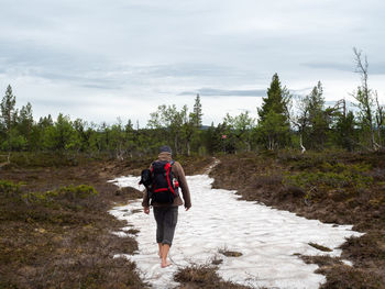 Rear view of man walking on snow against sky