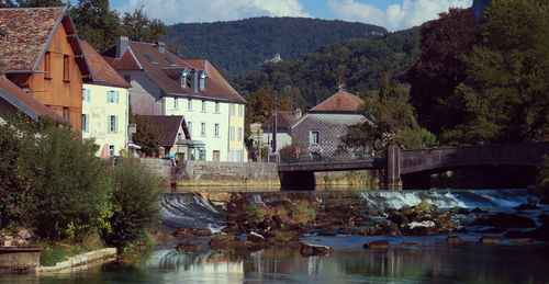 Houses by river and trees against sky