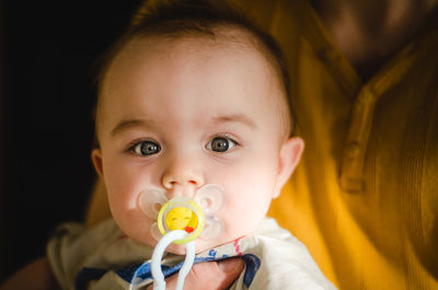 Portrait of cute baby girl with pacifier held by mother at home