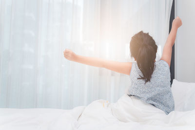 Back side of little girl stretching in bed after waking up, good morning world concept