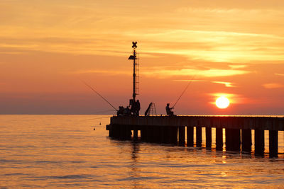 Silhouette pier over sea against orange sky