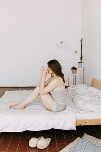 A happy girl in pajamas drinks coffee looks at the phone using technology while lying in bed at home