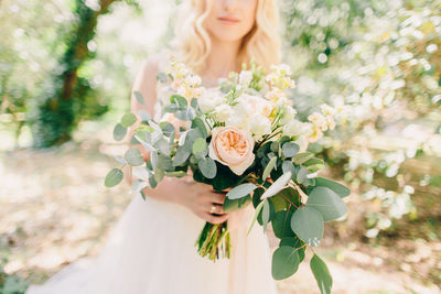 Midsection of bride holding flower bouquet while standing at park