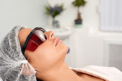 Portrait of smiling young woman wearing sunglasses on bed at home