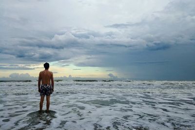 Rear view of shirtless young man standing at beach