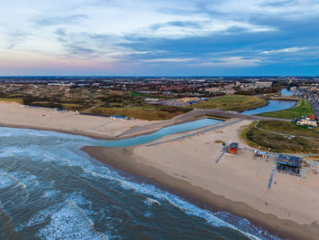 Aerial view of coastal town with sandy beach, canal flowing into ocean, and urban zone sunrise hues