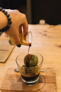 Midsection of person pouring drink in glass on table