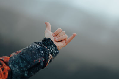 Unrecognizable male hand wearing a coat making the hang loose sign on top of a mountain background