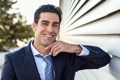 Portrait of smiling businessman leaning by blinds