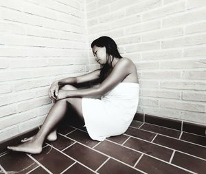 Side view of woman sitting against wall